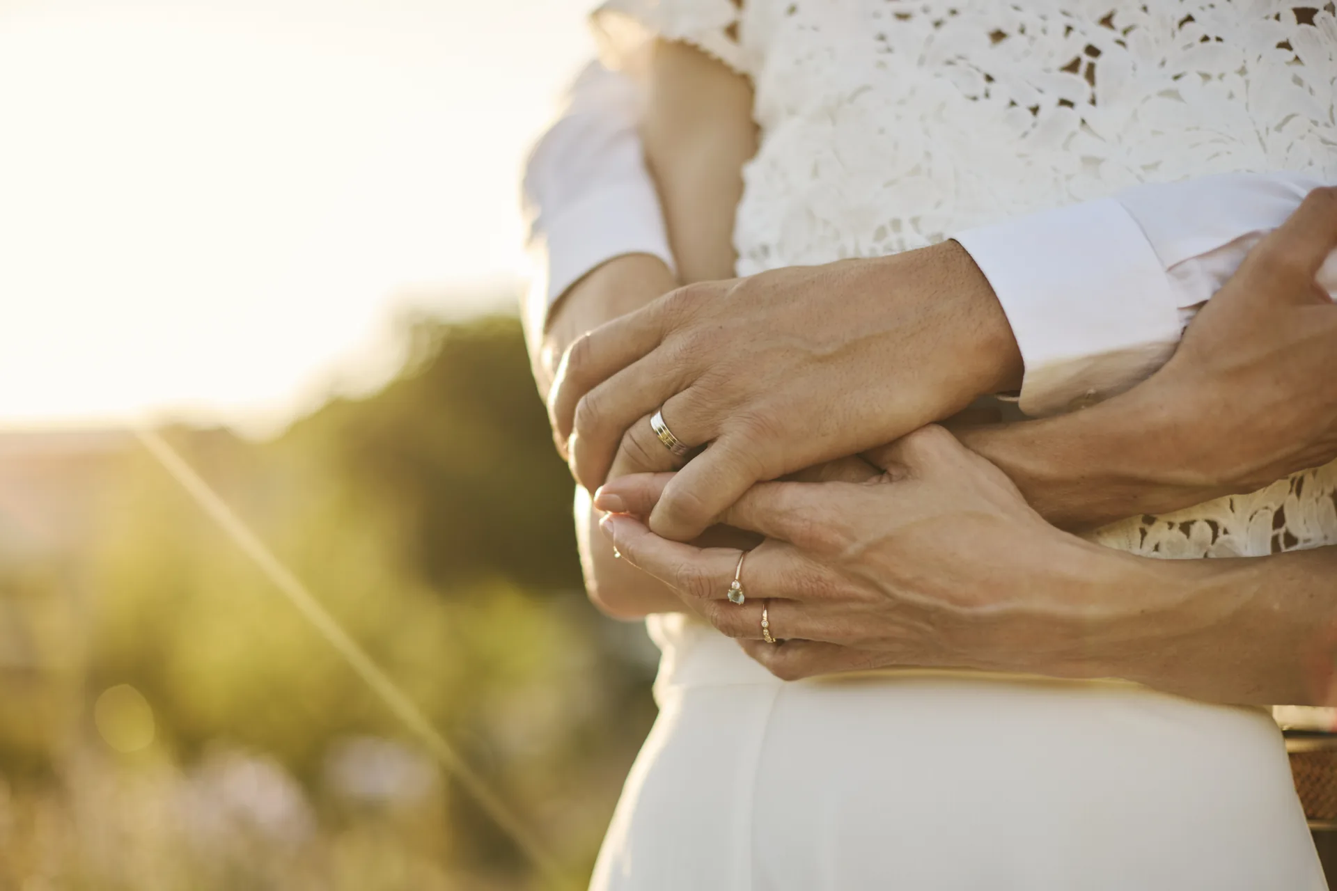 Un couple marié s'enlaçant avec des alliances visibles au coucher du soleil