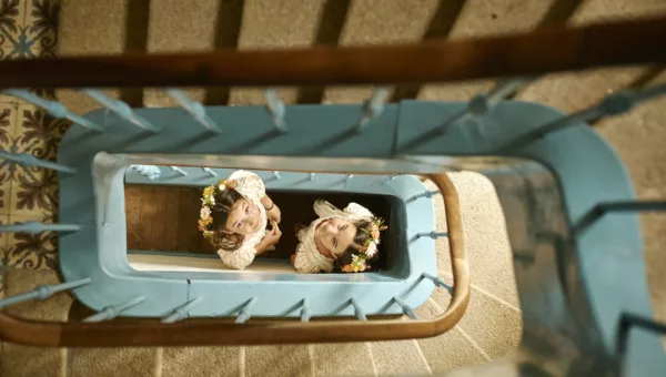 Deux petites filles en robes blanches avec des couronnes de fleurs regardant vers le haut dans une cage d'escalier bleue